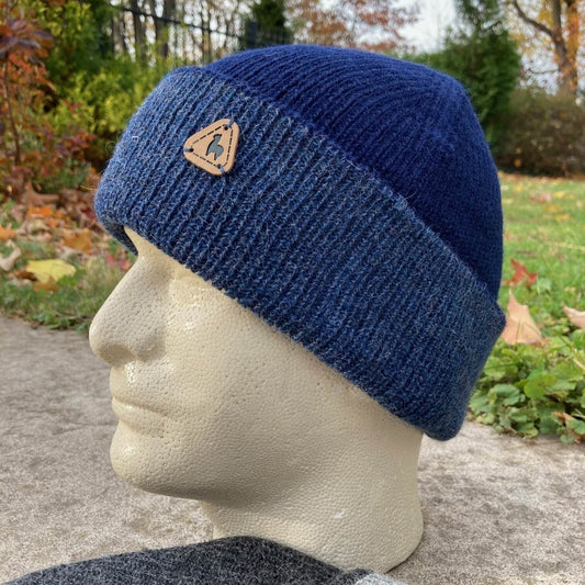 Blue knit alpaca hat with a logo on a mannequin head outdoors.