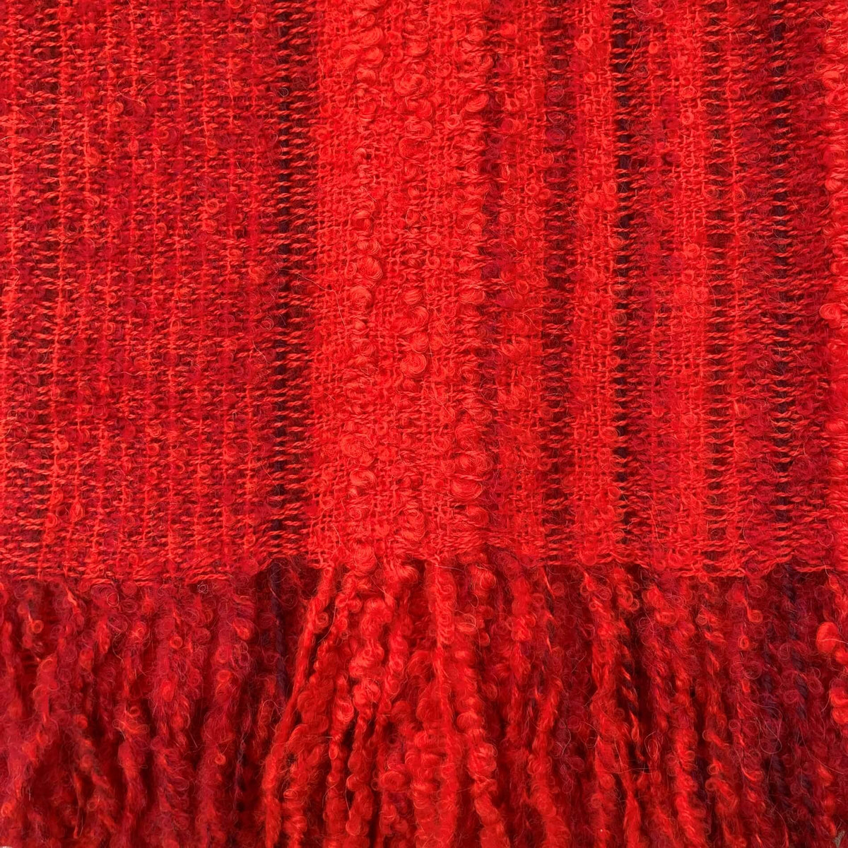 A close-up of a vibrant red woven fabric with vertical textured stripes and a matching red tassel fringe along the bottom edge.