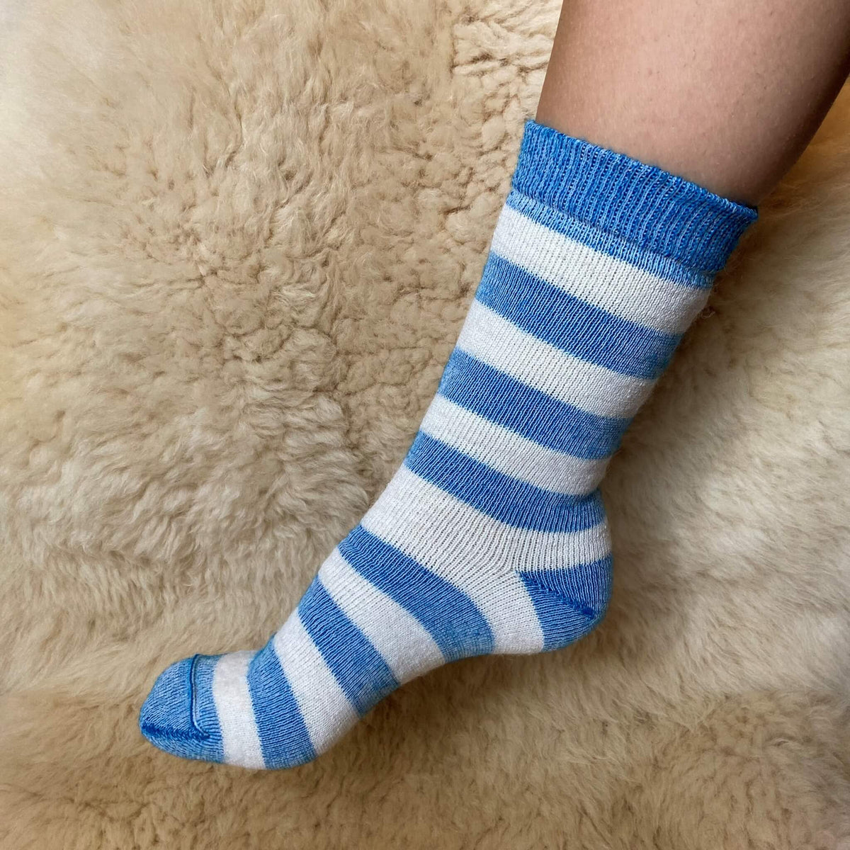 A person's foot wearing a blue and white striped knit sock, resting on a beige alpaca fur surface.