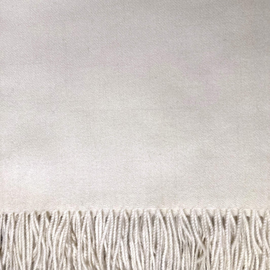 Close-up of an ivory white woven textile with a fringe along the bottom edge.