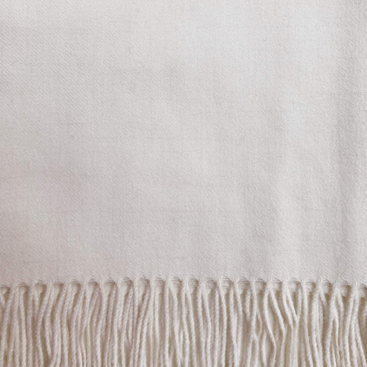 A close-up of soft ivory woven textile with fringe along the bottom edge.
