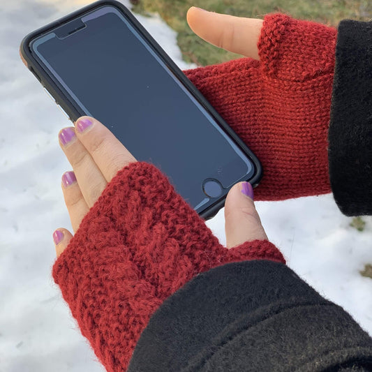 Burgundy fingerless knit gloves worn on hands, holding a black smartphone outdoors over snow.