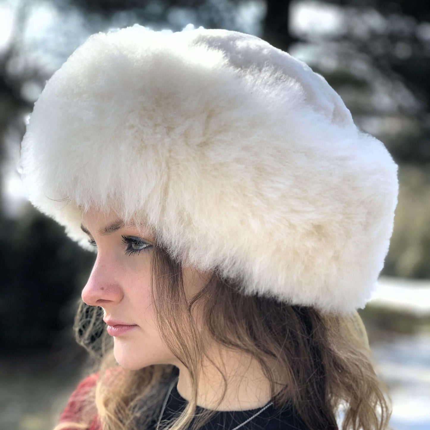 Woman wearing light beige Russian style alpaca fur hat with a blurred background.