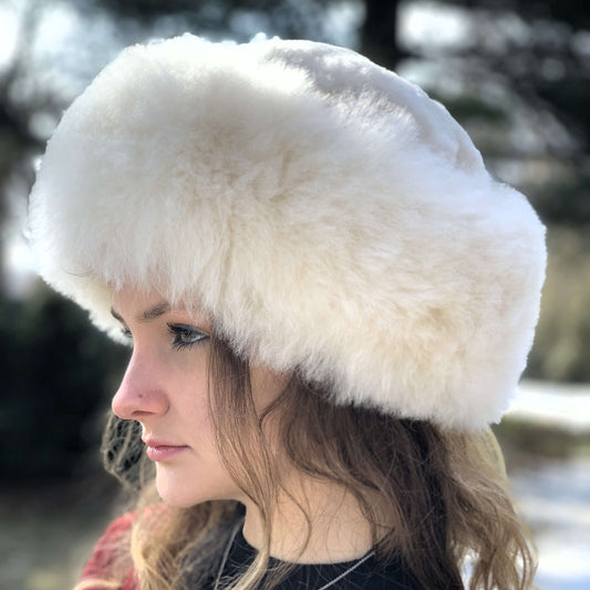 Woman wearing light beige Russian style alpaca fur hat with a blurred background.