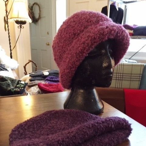 Mannequin head wearing plum coloured alpaca hat knit with boucle yarn with other hats in background.