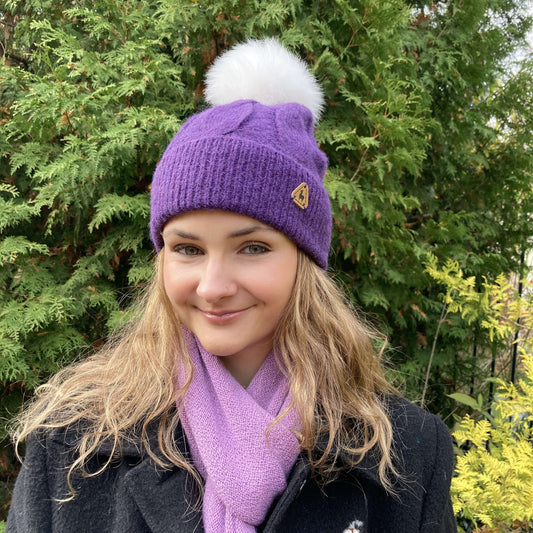 Woman wearing a purple alpaca cable knit hat with a white alpaca fur pom-pom and purple alpaca scarf outdoors.