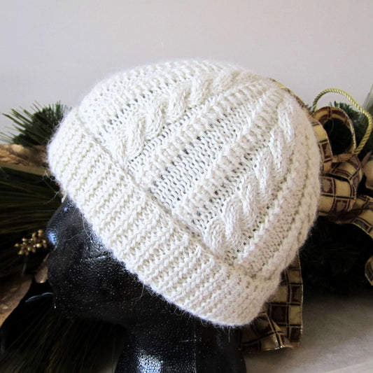 Ivory cable knit alpaca hat on a mannequin head with decorative elements in the background
