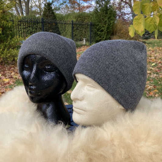 Two mannequin heads wearing grey alpaca hats outdoors with greenery in the background.