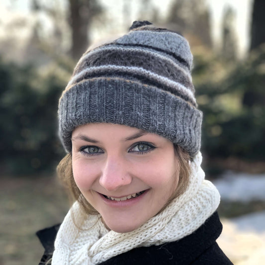 Woman wearing a gray patterned knit alpaca hat and white alpaca scarf outdoors with blurred background