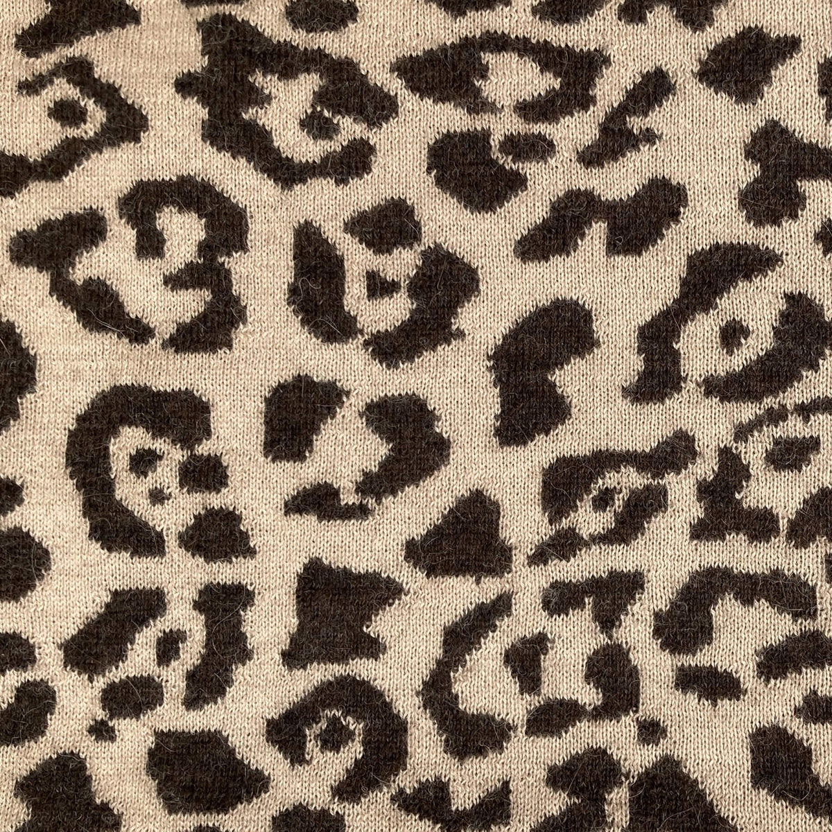 Close-up of a leopard print fabric texture with dark brown irregular spots on a warm beige background.