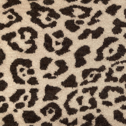 Close-up of a leopard print fabric texture with dark brown irregular spots on a warm beige background.