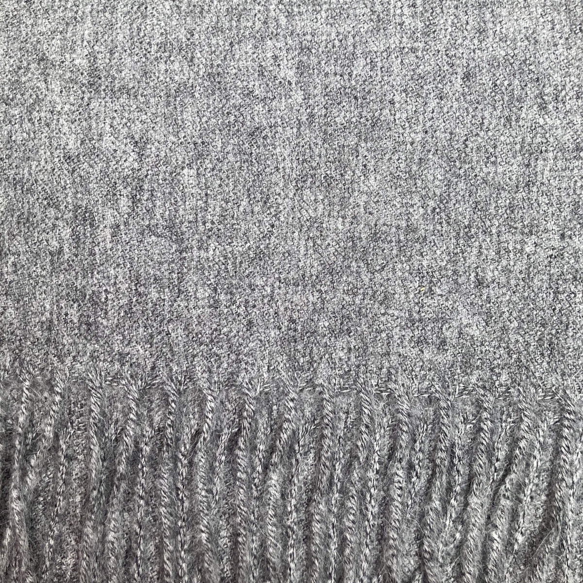 Close up of mottled black, grey, and ivory woven fabric with fringe on the bottom.