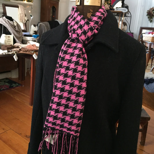 A pink and black houndstooth scarf with fringe, styled on a black coat mannequin in a retail store.