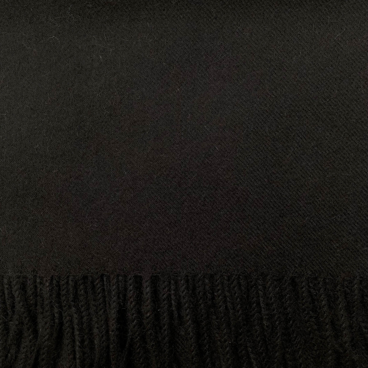 A close-up of a black woven textile with a fringe along the bottom edge.