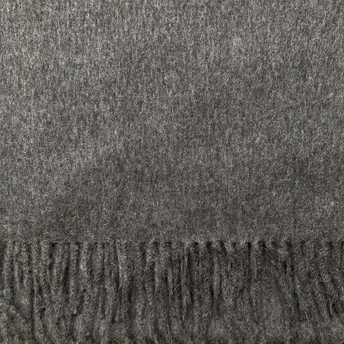 A close-up of a dark grey textured fabric with a fringed edge along the bottom.
