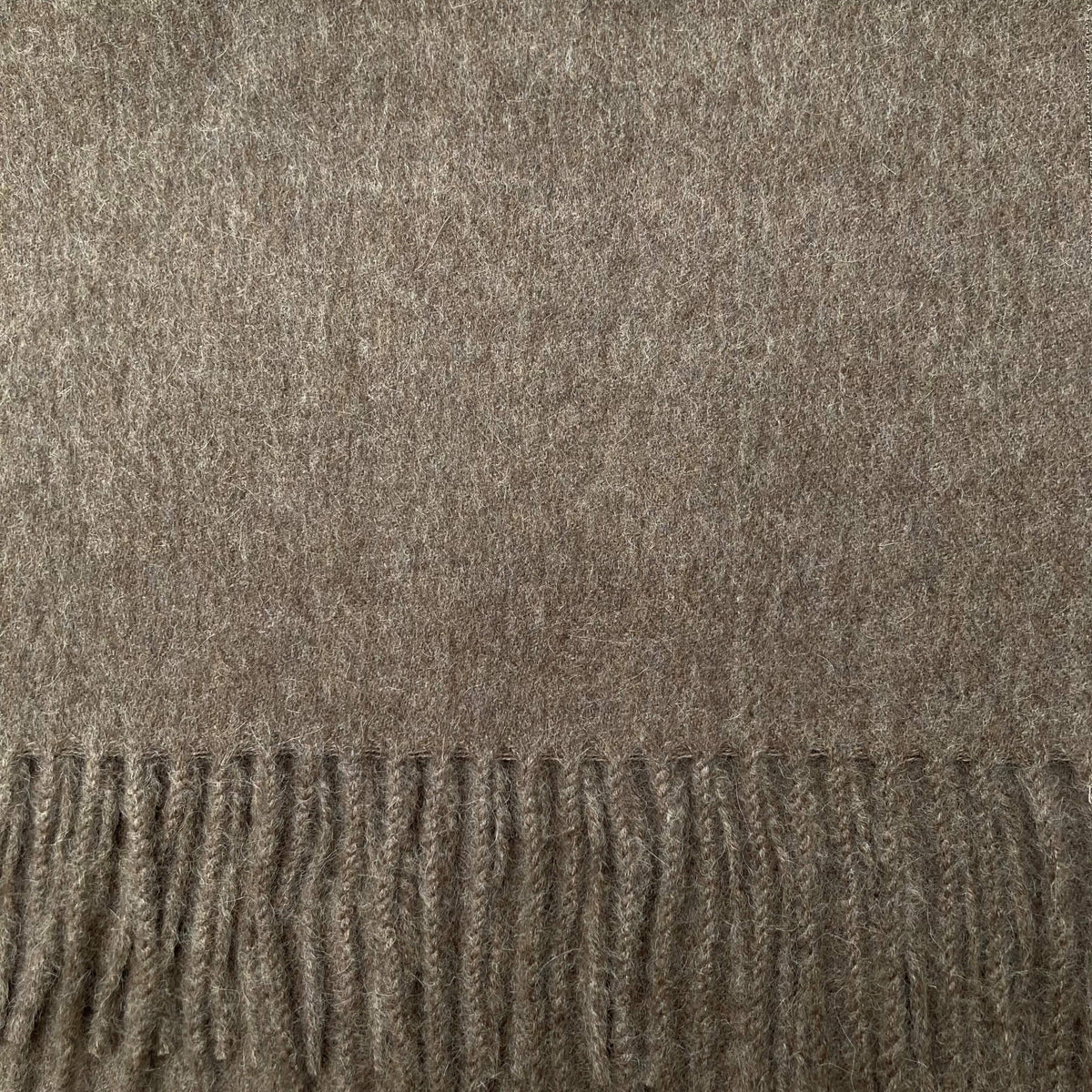 A close-up of a textured woven fabric in a heather taupe-brown color, showing the material's fine woven pattern and a fringed edge along the bottom.