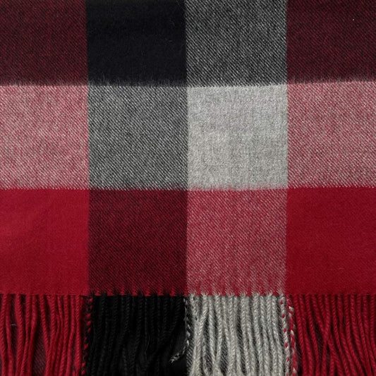 A close-up of a plaid scarf with red, black, gray, and white check blocks and fringed edges.