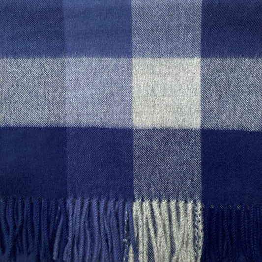 A close-up of a woven plaid scarf with fringed edges, featuring navy blue, medium blue, and light gray-blue checks.