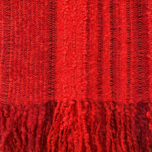 A close-up of a vibrant red woven fabric with vertical textured stripes and a matching red tassel fringe along the bottom edge.