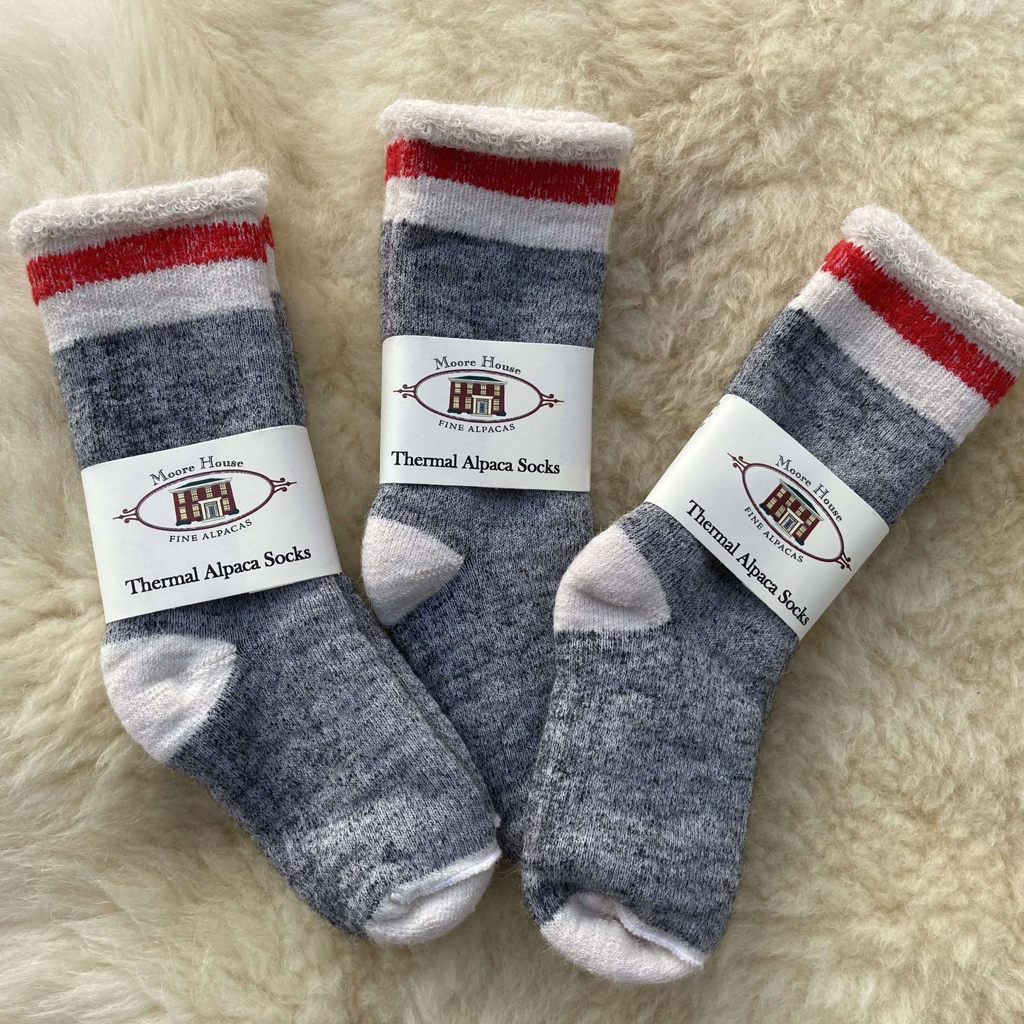 Three pairs of thermal alpaca socks on a fluffy white surface with labels.