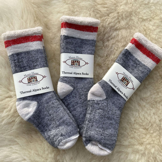 Three pairs of thermal alpaca socks on a fluffy white surface with labels.