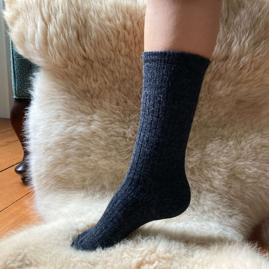 Charcoal grey ribbed alpaca sock on a fluffy beige surfac