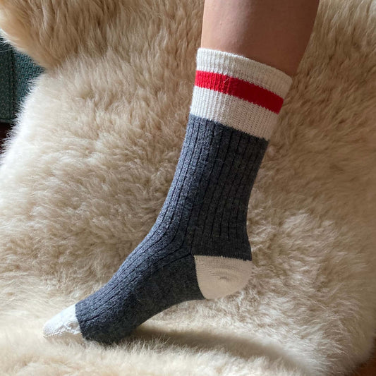 Gray alpaca work sock with a red stripe on a fluffy beige surface