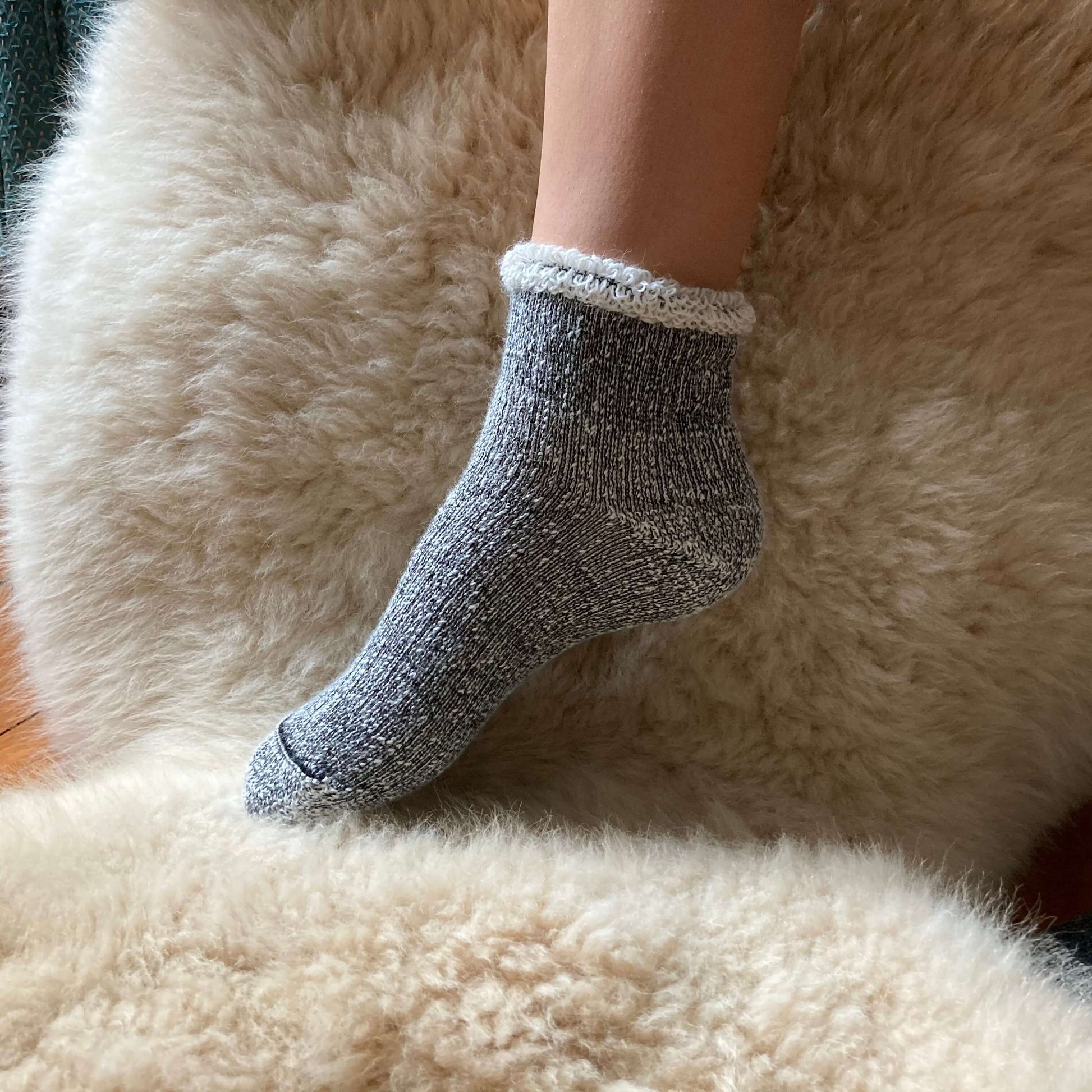 Ankle length grey alpaca sock on a fluffy surface