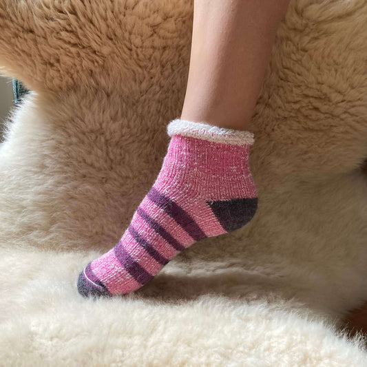 Ankle length pink striped alpaca sock on a fluffy surface