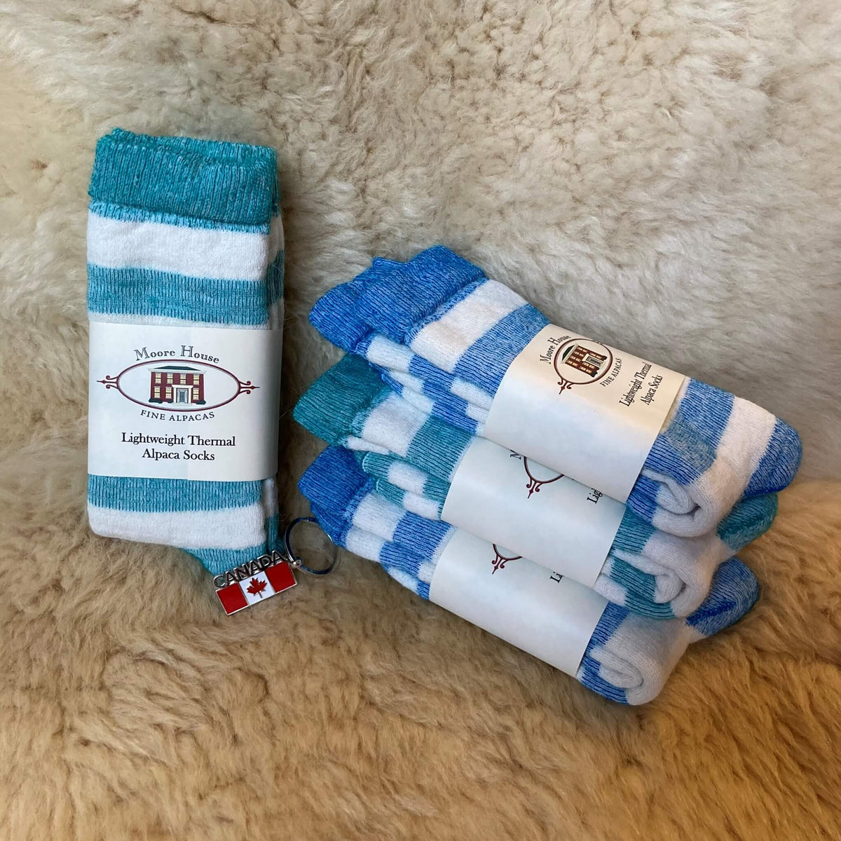 Four packaged pairs of striped alpaca socks on a fluffy alpaca fur rug. Two sock pairs are blue and white striped and the other two pairs are green and white striped.