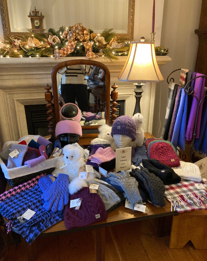 Display of knitted alpaca hats and alpaca scarves on a table with a fireplace and mirror in the background.