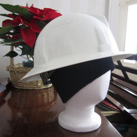 Mannequin head wearing a white hard hat with a dark charcoal grey ribbed knit alpaca hat underneath with a red flower in the background.