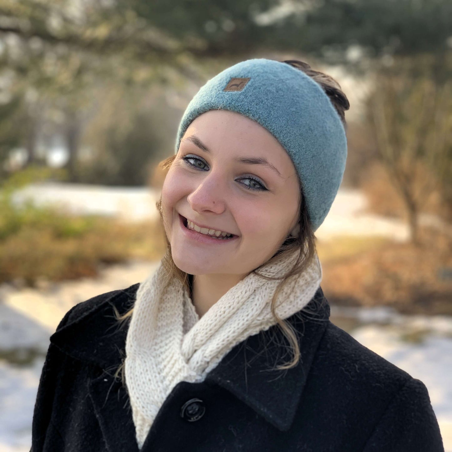 Woman wearing a light aqua green alpaca knit headband and an ivory knit scarf with a blurred outdoor winter background.