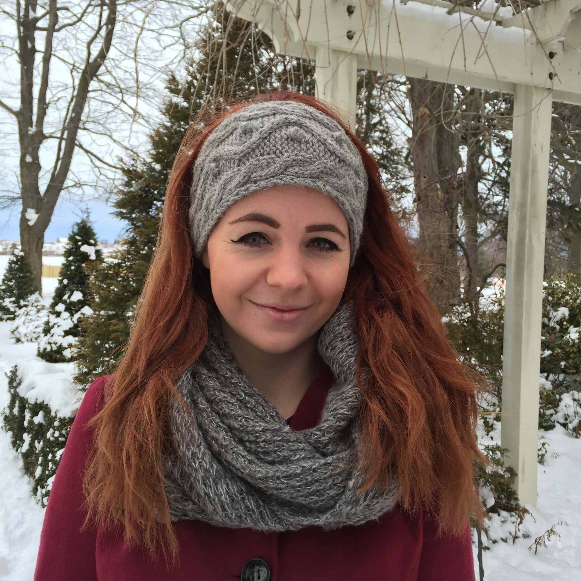 Woman wearing a cable knit alpaca headband in grey with winter background.