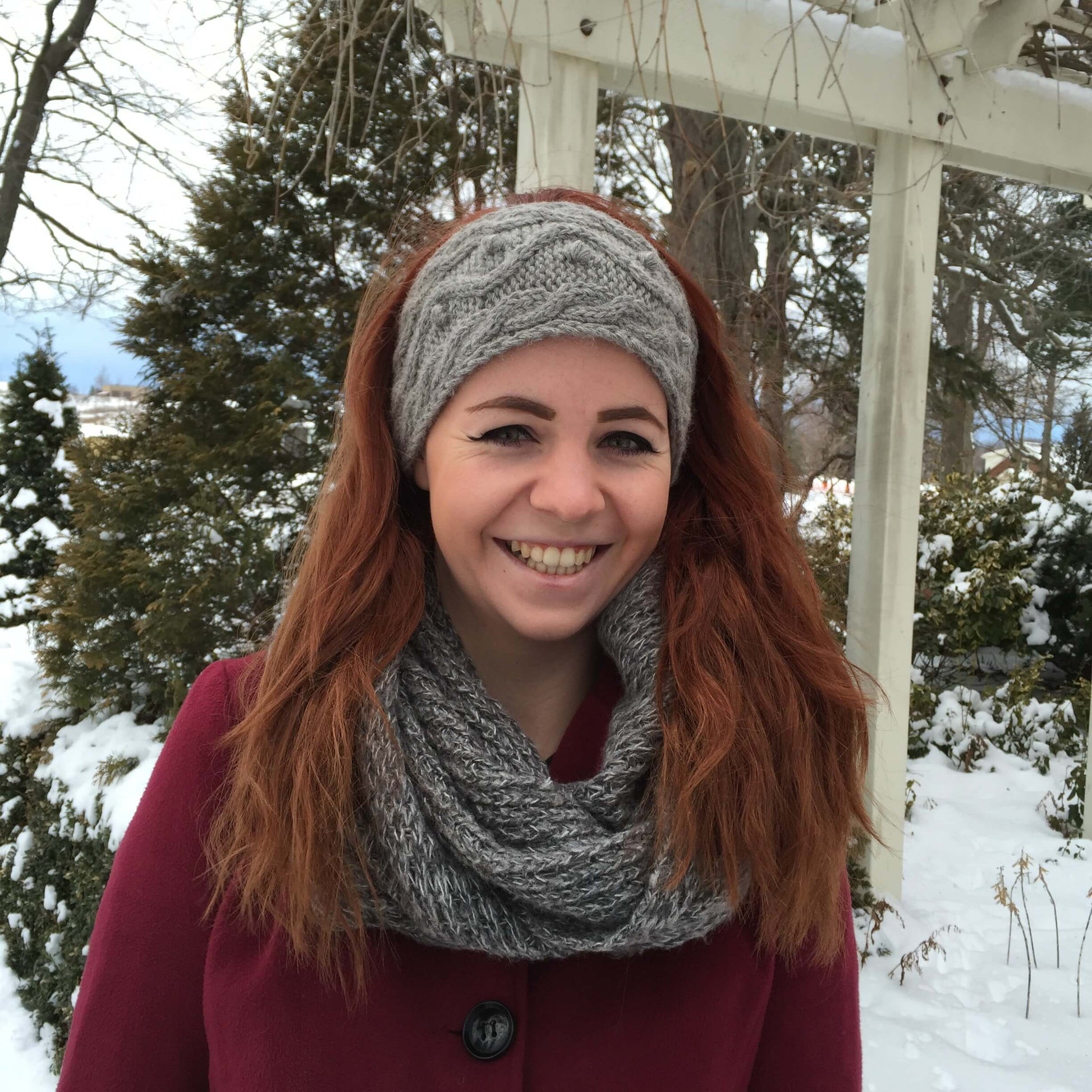 Woman wearing a cable knit alpaca headband in grey with winter background.