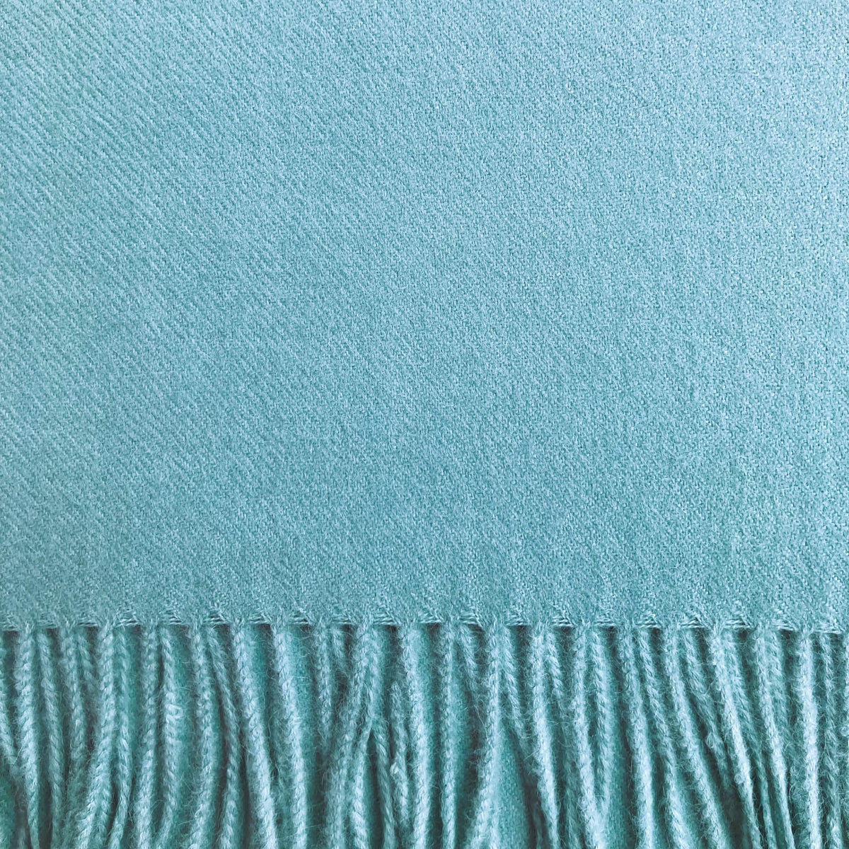 Close up of aqua green woven fabric with fringe on the bottom.