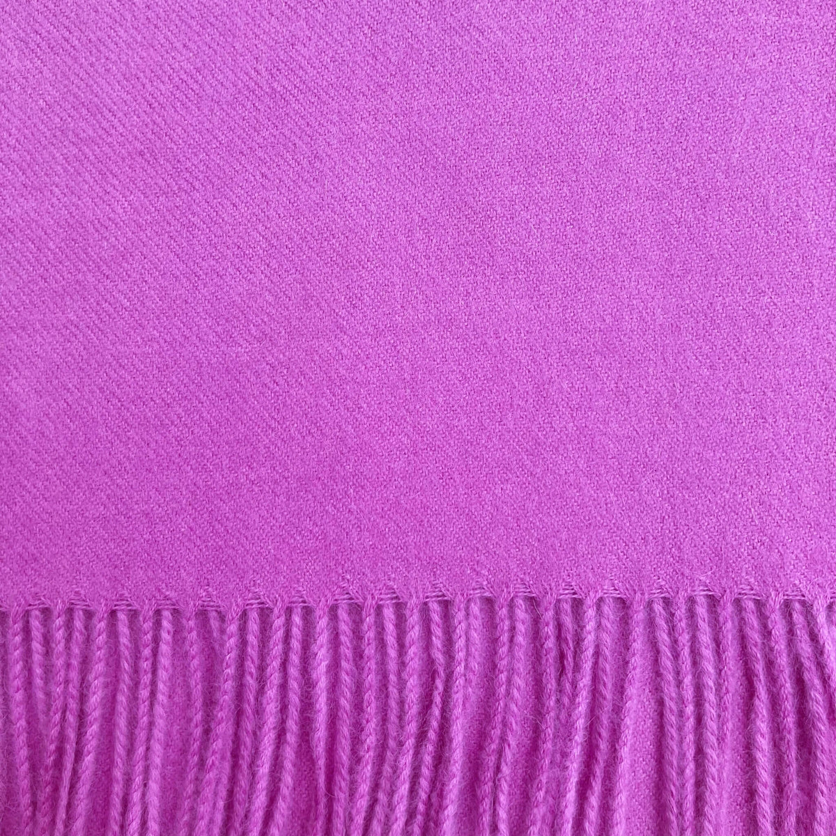 Close up of fuchsia pink woven fabric with fringe on the bottom.