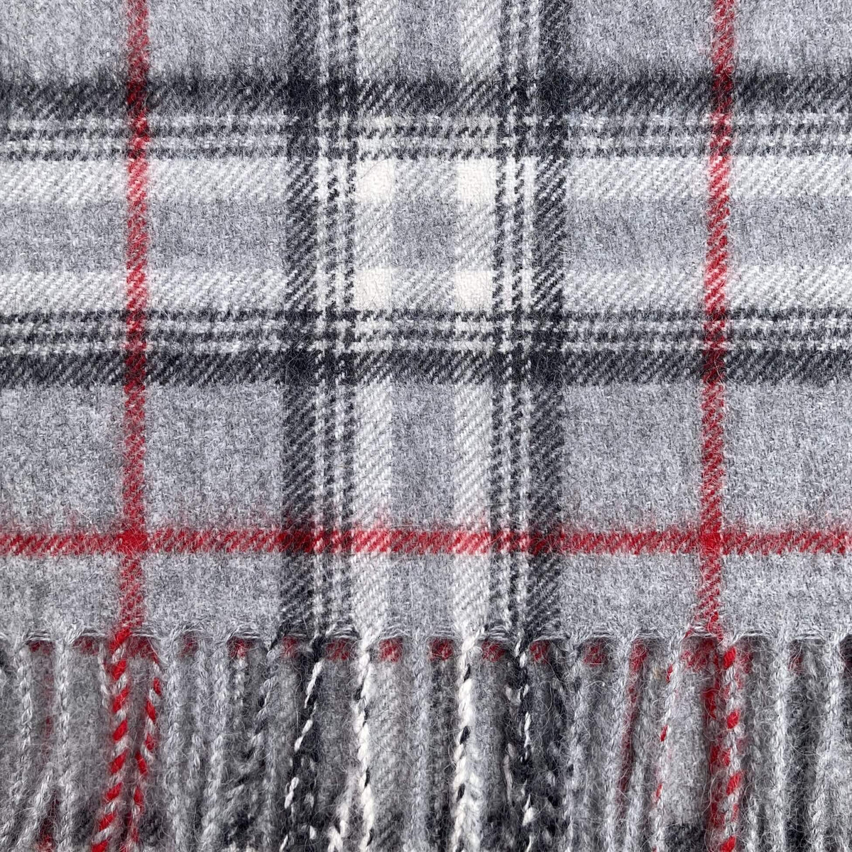 Close up of charcoal grey, silver grey, ivory, and red plaid woven fabric with fringe on the bottom.