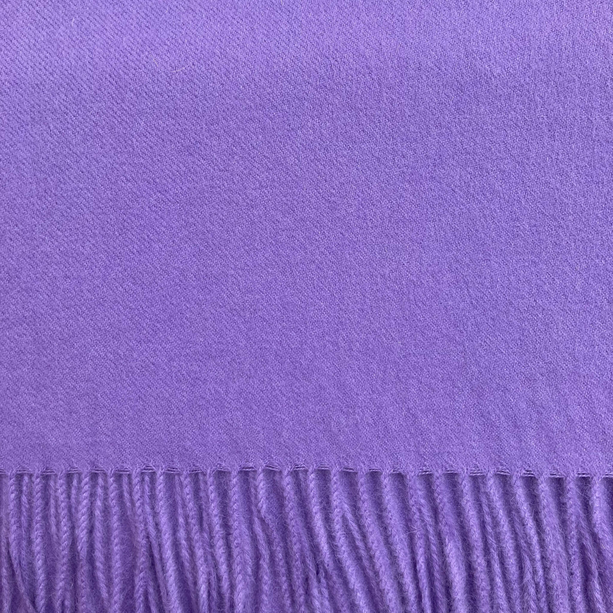 Close up of violet woven fabric with fringe on the bottom.