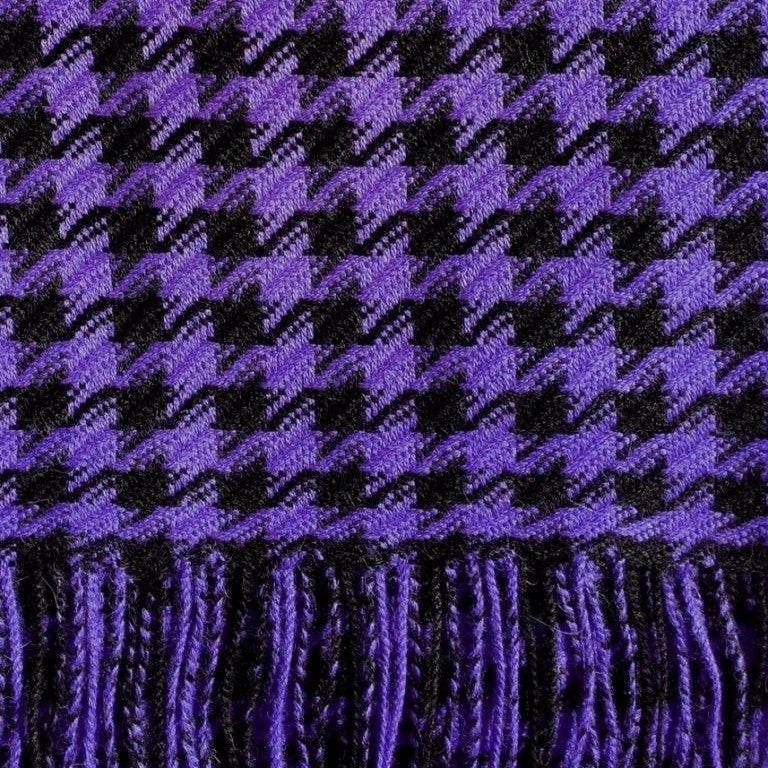 A close-up of a periwinkle purple and black houndstooth patterned fabric with fringed edges.