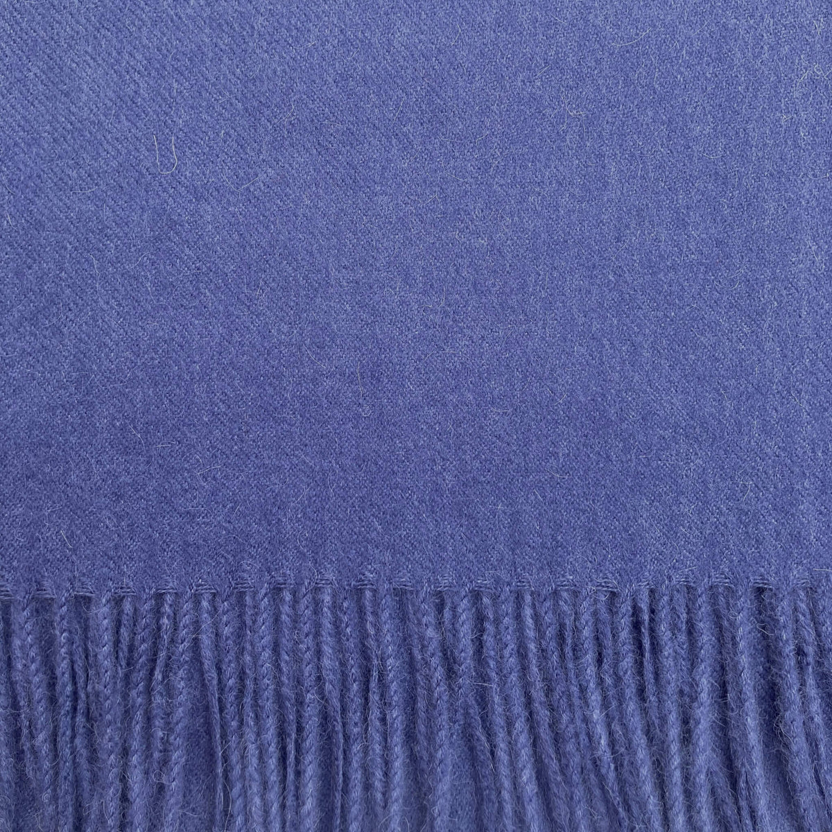 A close-up of a textured blue-purple woven fabric with a fringed edge along the bottom.