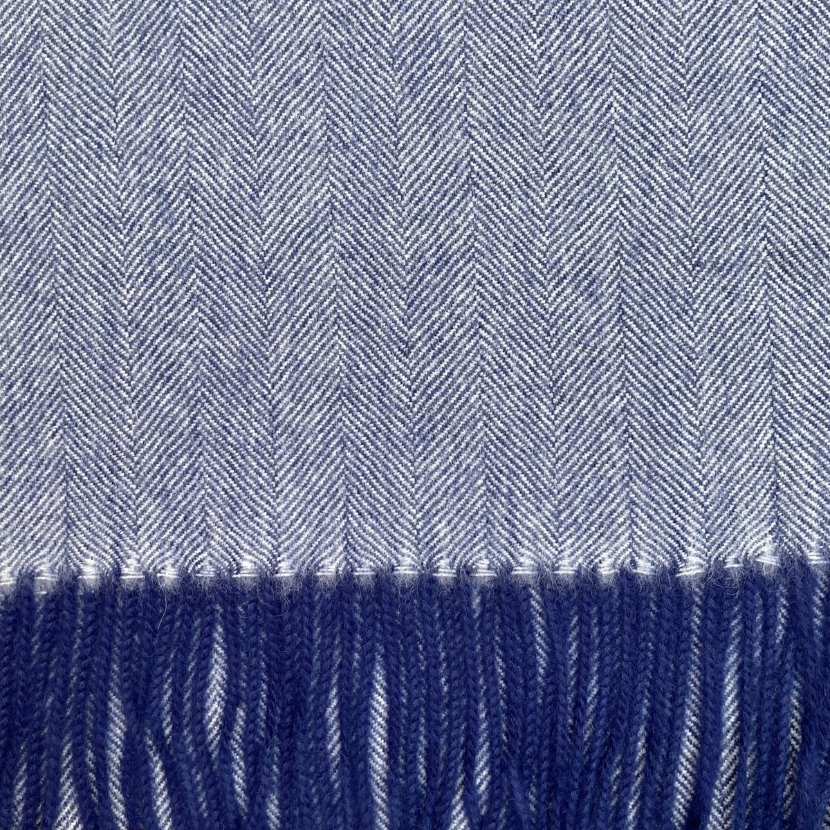 Close up of blue and ivory woven fabric in a herringbone pattern with blue fringe on the bottom.