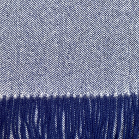 Close up of blue and ivory woven fabric in a herringbone pattern with blue fringe on the bottom.