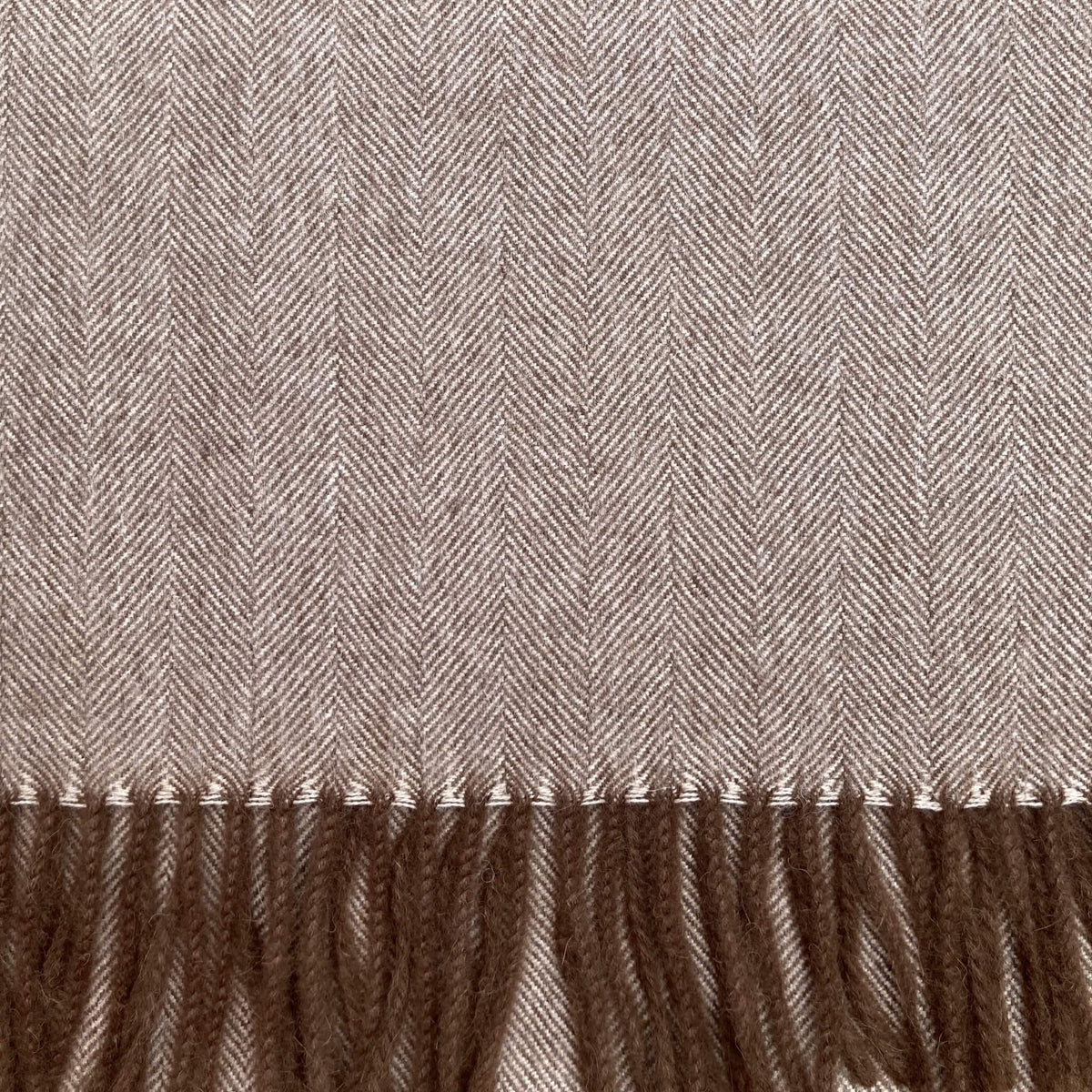 Close up of brown and beige woven fabric in a herringbone pattern with brown fringe on the bottom.