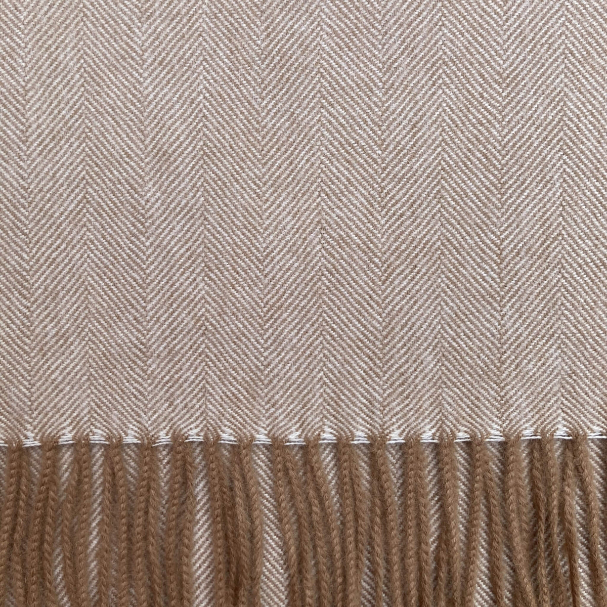 Close up of camel brown and ivory woven fabric in a herringbone pattern with camel brown fringe on the bottom.