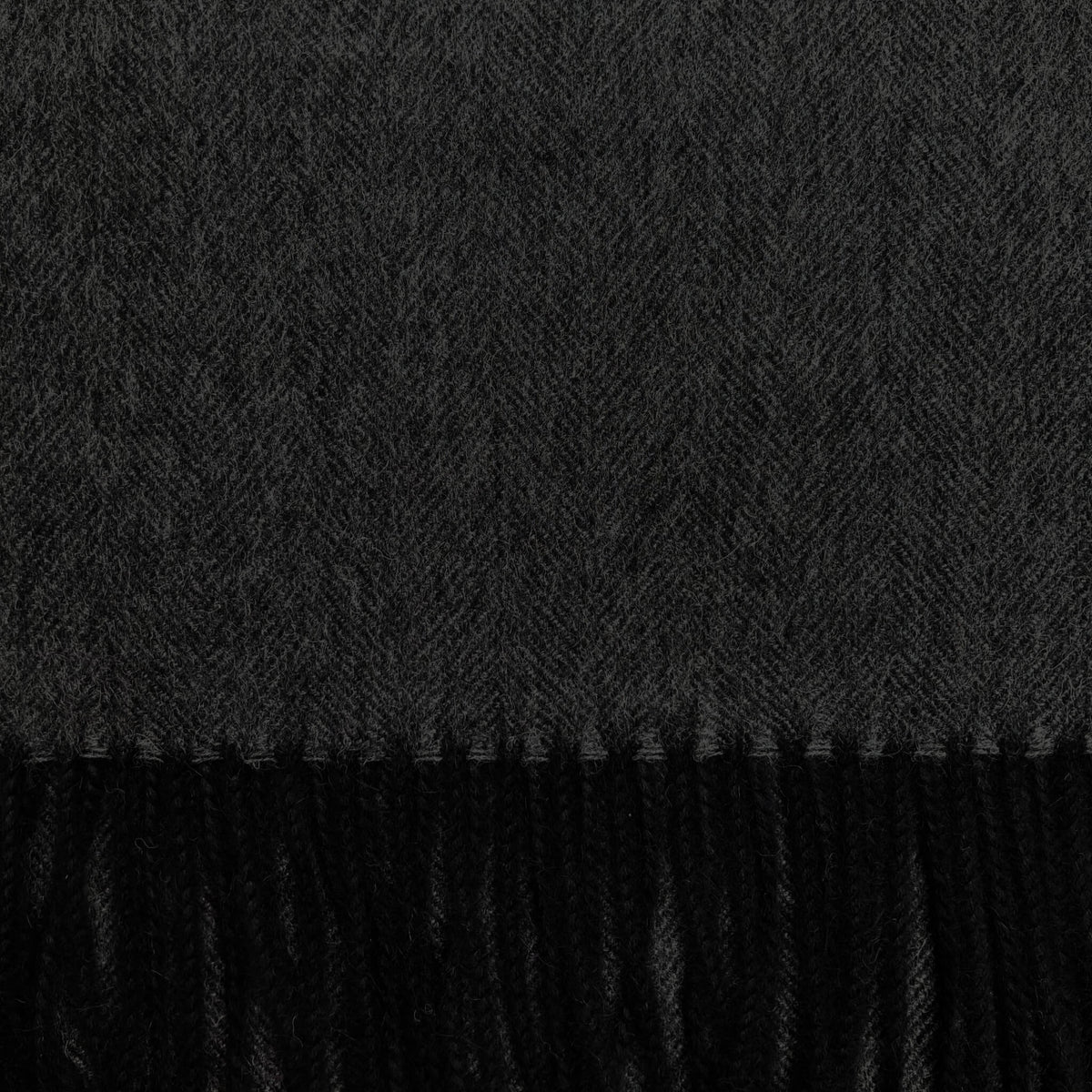 Close up of black and grey woven fabric in a herringbone pattern with black fringe on the bottom.