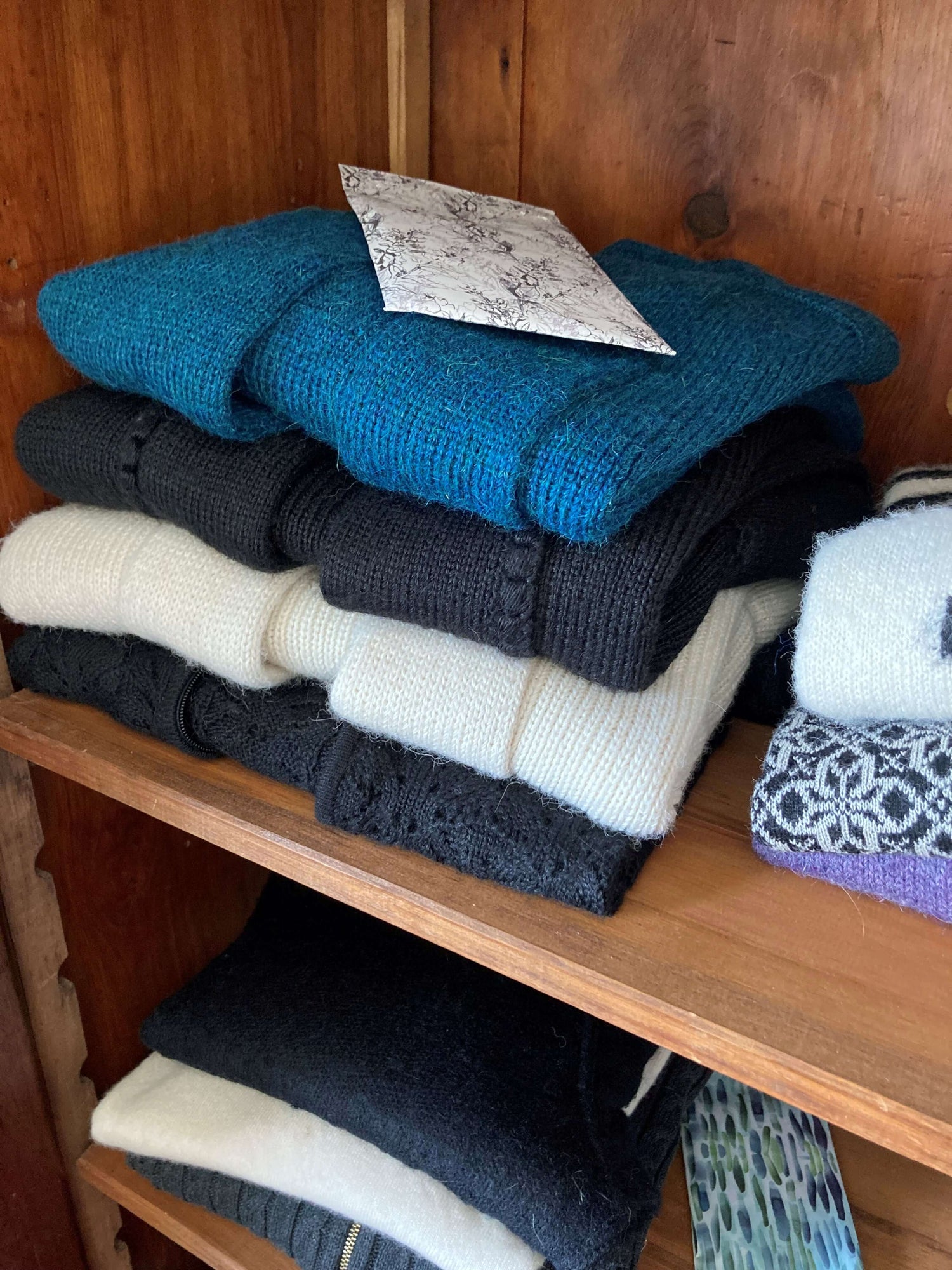 A stack of 4 alpaca sweaters on a wooden shelf in a wooden wardrobe.