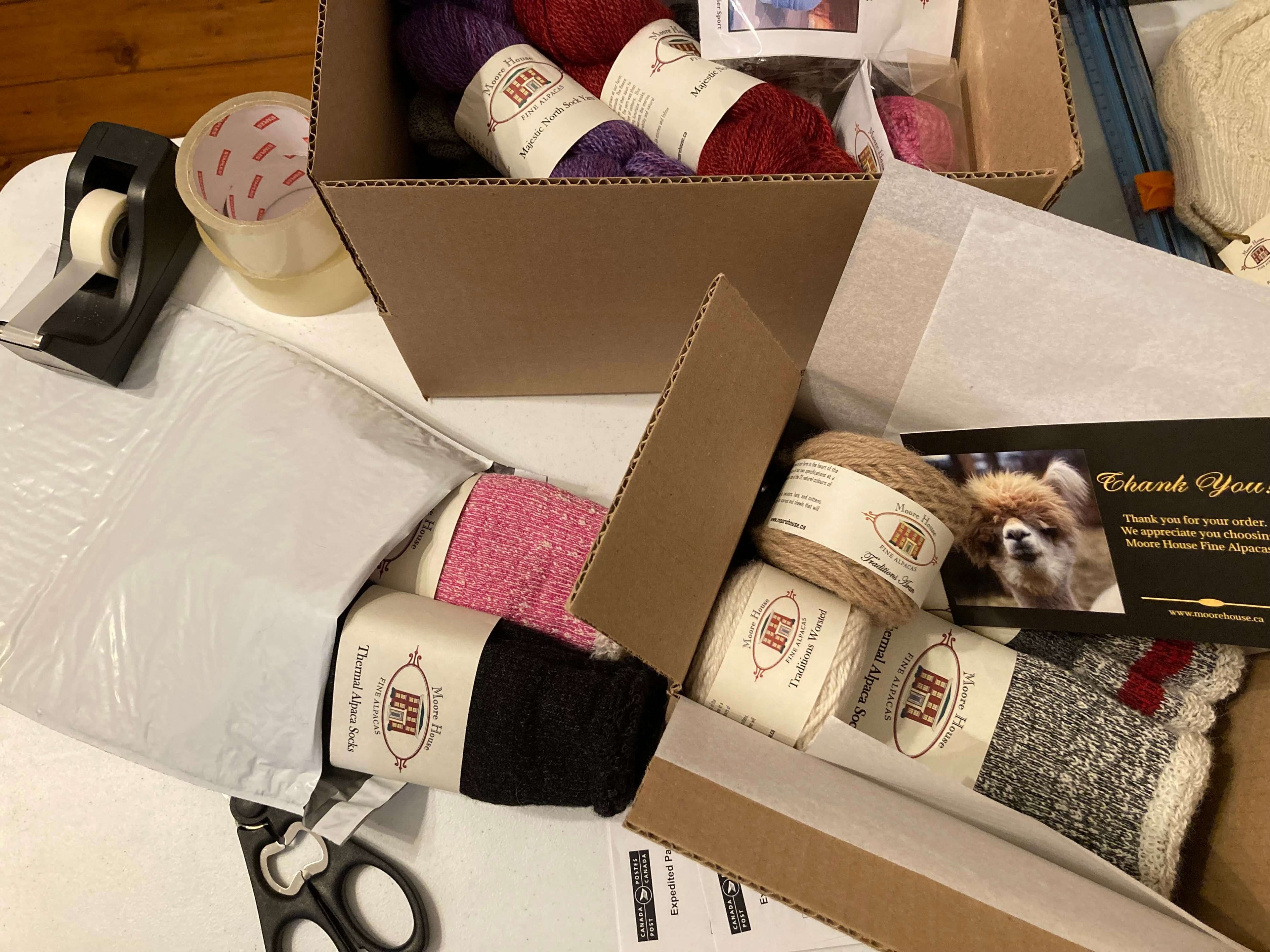 Shipping Box containing alpaca yarn and alpaca socks with shipping supplies including scissors and tape.