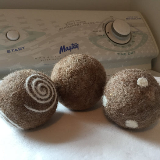 Three brown felted alpaca dryer balls in front of a Maytag dryer.