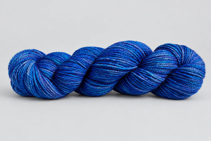 Skein of blue yarn with variegations of shades of blue on white background